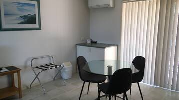 A small, clean room with a glass table, two chairs, a metal drying rack, a cabinet, and a window with blinds.