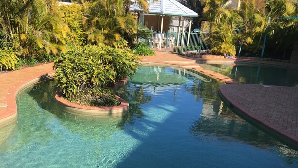 A clear swimming pool with a hot tub area, surrounded by lush greenery and a covered seating area. - Town Beach Beachcomber Resort (Port Macquarie)
