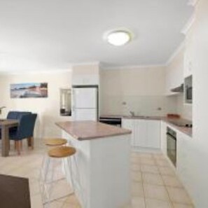 A compact kitchen with a central island, a dining area with chairs, and a small bar area. - Town Beach Beachcomber Resort (Port Macquarie)