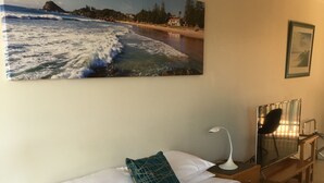 A hotel room with a bed, a nightstand, a desk with a chair, a lamp, and a painting of a beach scene. - Town Beach Beachcomber Resort (Port Macquarie)
