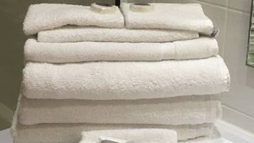 A stack of white towels and two bottles of Elements shampoo and conditioner on a white surface.