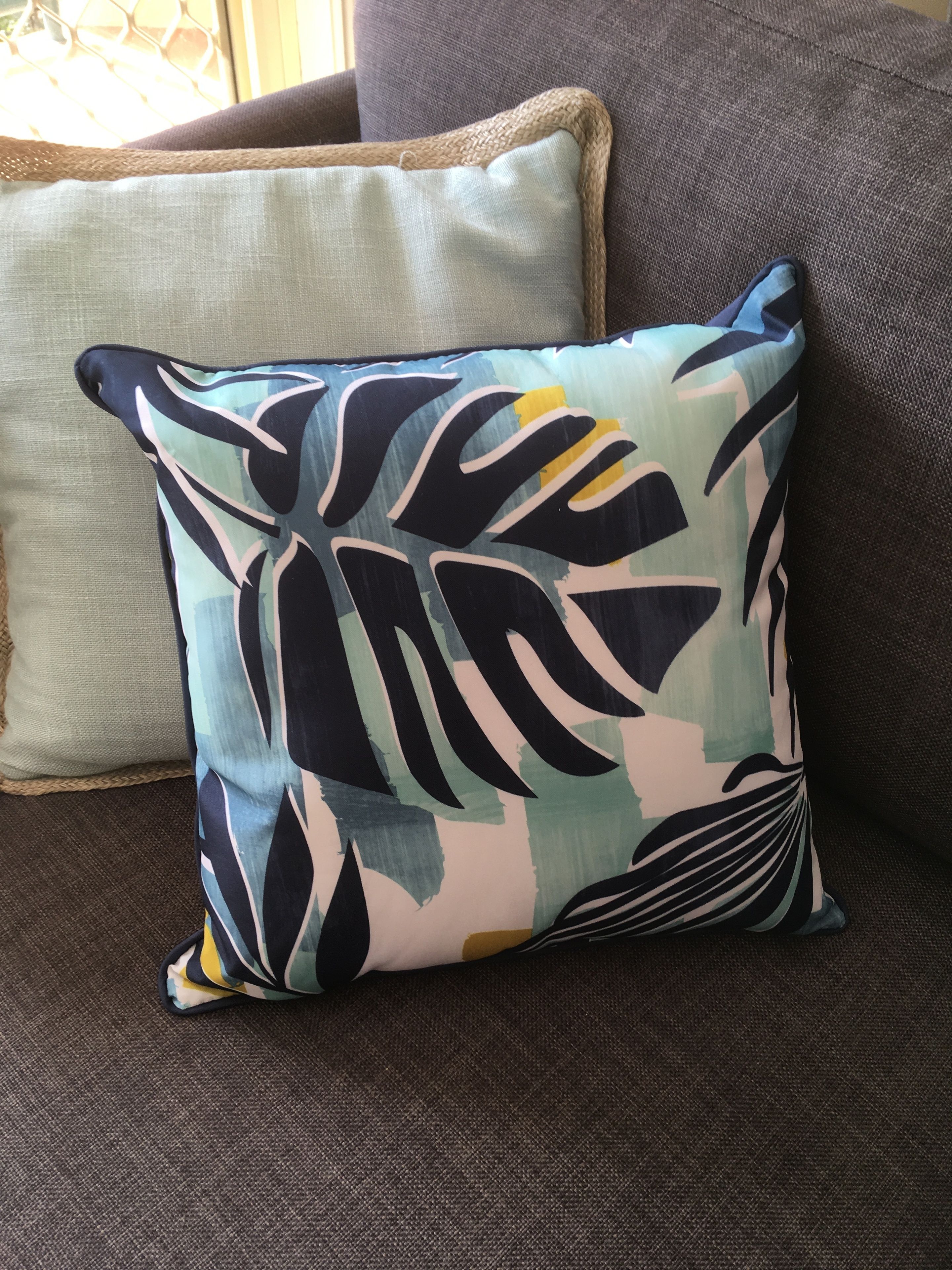 Un sofá con dos almohadas, una con estampado de hojas y la otra lisa.