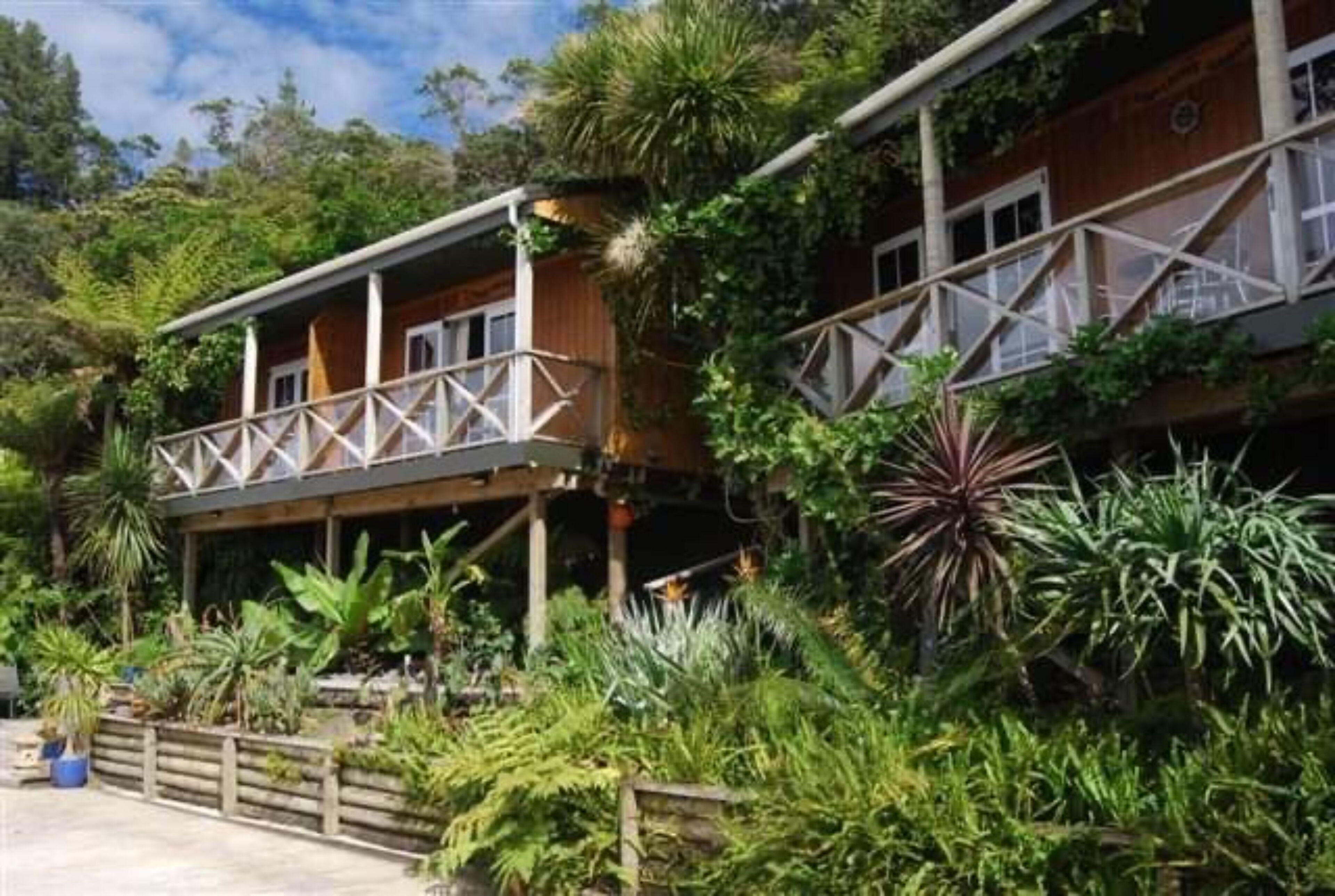 Un bâtiment en bois à deux étages, doté d’un balcon et entouré d’une végétation tropicale luxuriante.