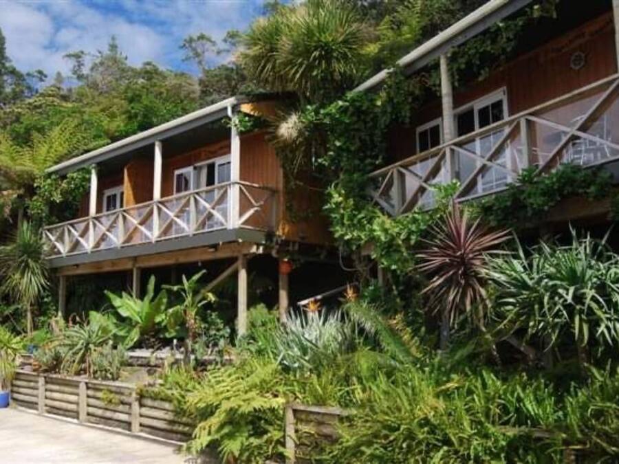 A two-story wooden building with a balcony, surrounded by lush tropical vegetation.