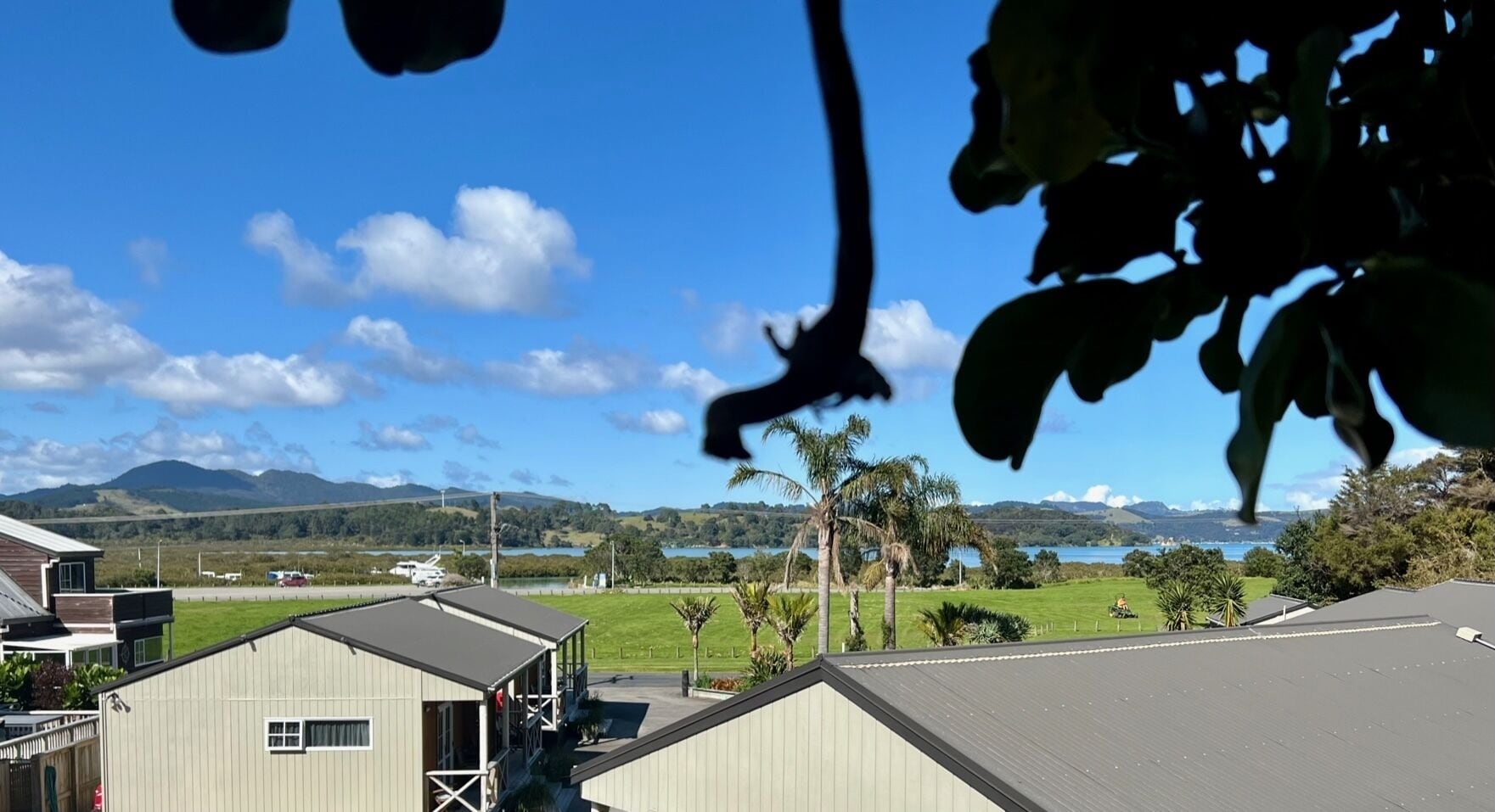 A view of a residential area with a house, a small building, and a distant lake.