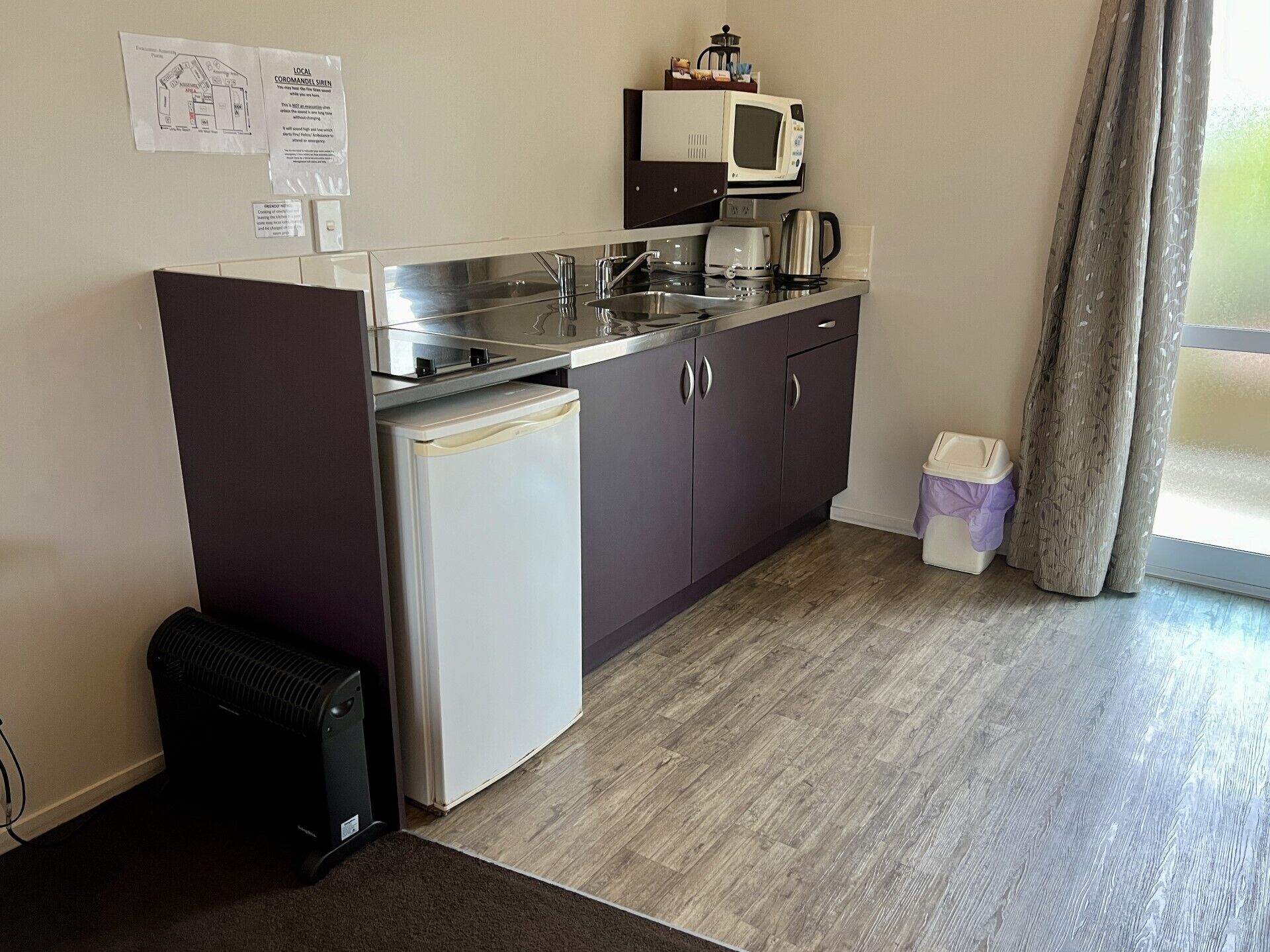 Una cocina compacta con refrigerador, estufa, fregadero y microondas. Hay armarios y un pequeño bote de basura.