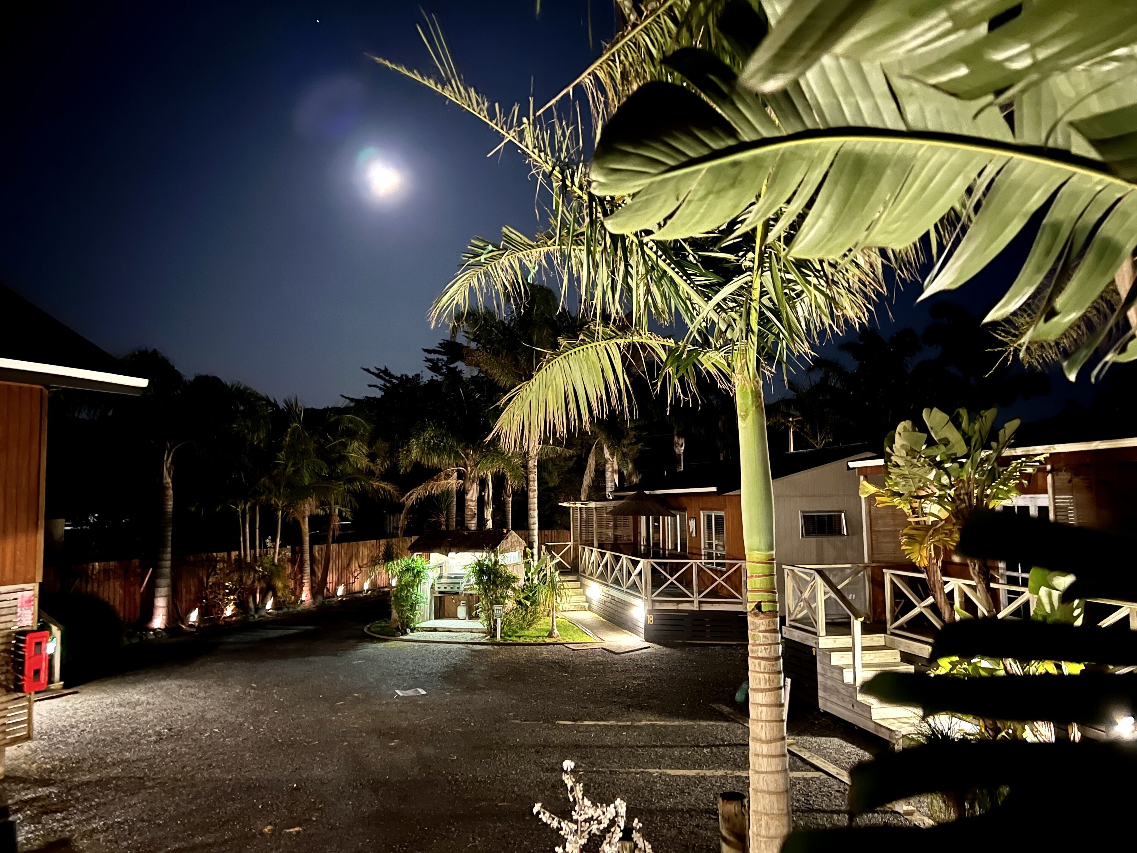 A nighttime view of a residential area with a well-lit pathway leading to a house with a wooden deck and a small porch.