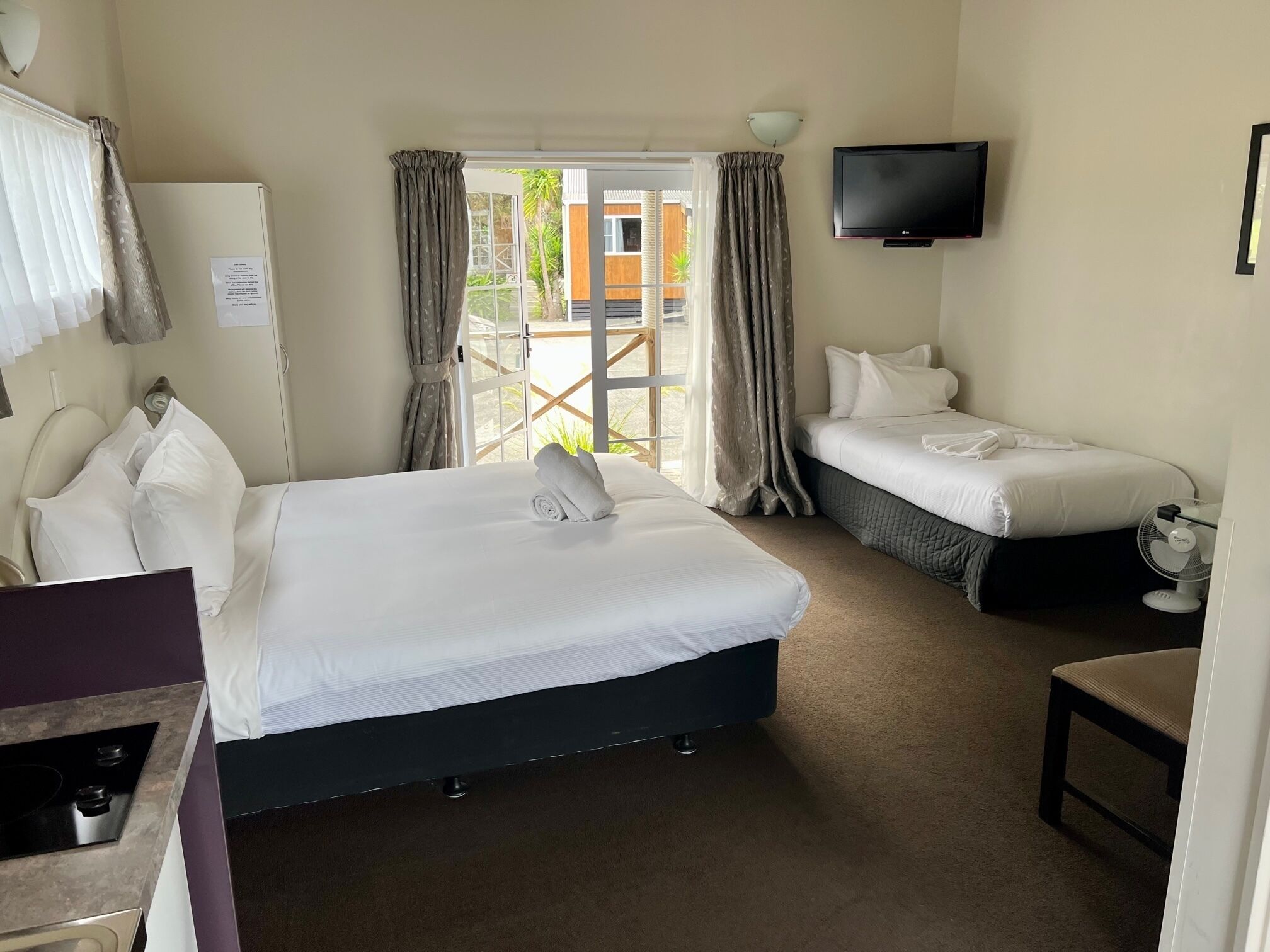 A hotel room with a large bed, a smaller bed, a TV, a desk, and a chair.