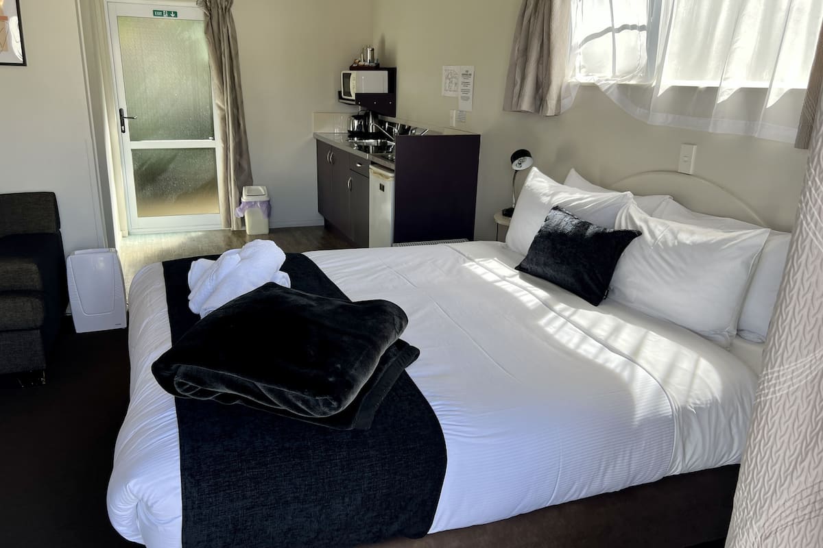 A hotel room with a bed, a desk, a microwave, and a window with curtains.