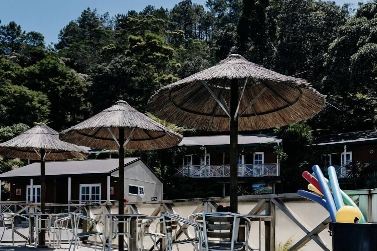 A swimming pool with a wooden deck, metal chairs, and thatched umbrellas.