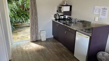 A compact kitchen with a microwave, sink, and dishwasher. There is a small trash bin and a fan near the sink.