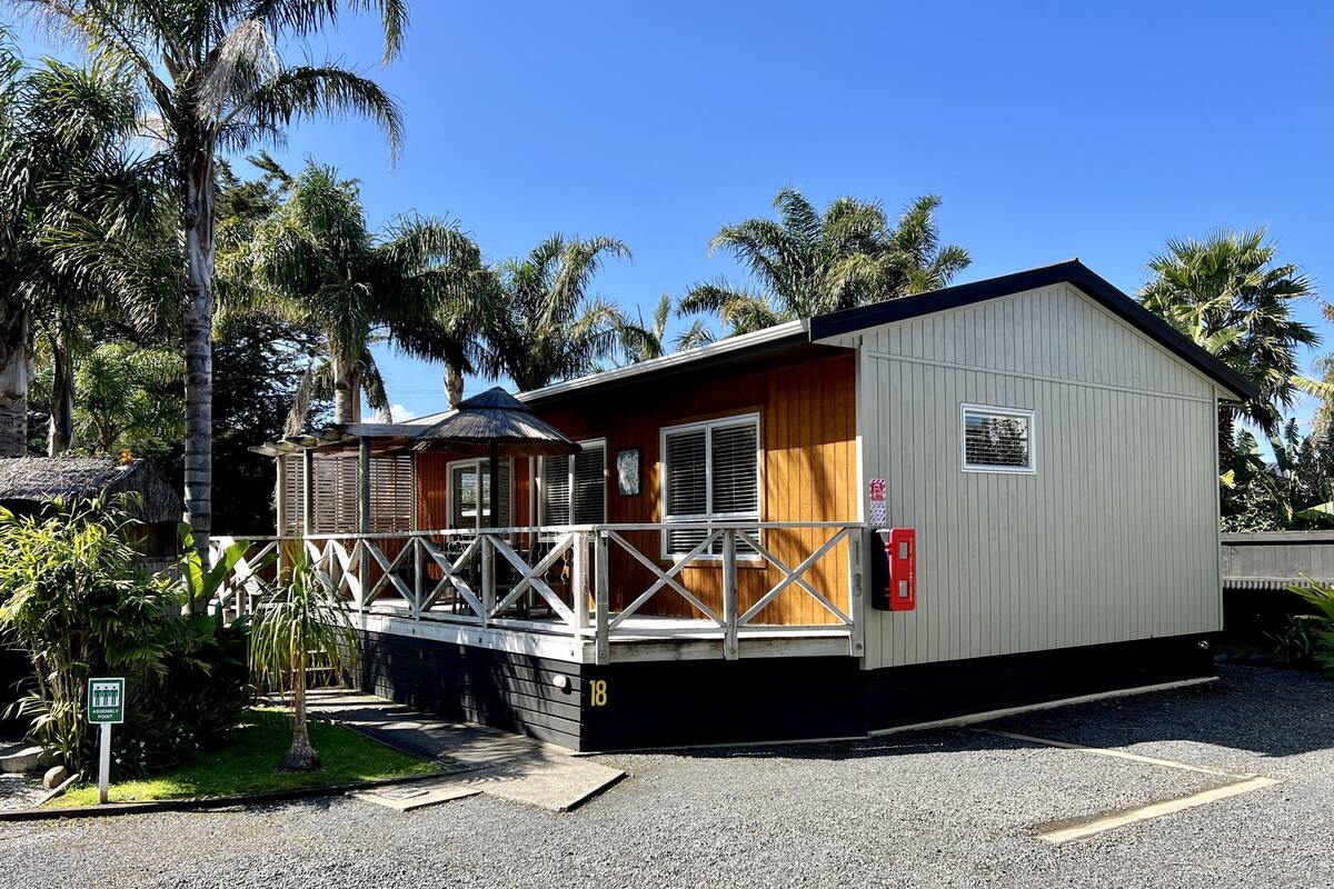 A small, single-story building with a porch and a covered area, surrounded by palm trees.