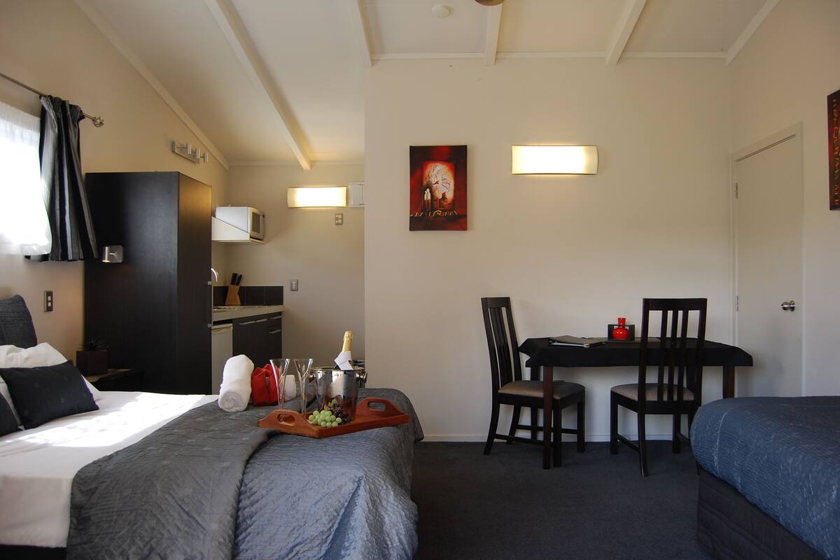 A hotel room with a bed, a desk, a chair, a microwave, and a painting on the wall.