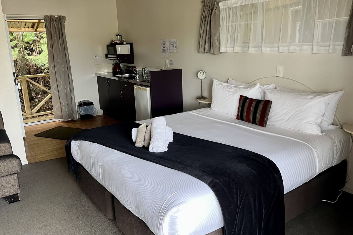 A hotel room with a bed, a desk, a chair, a small table, and a window with curtains.