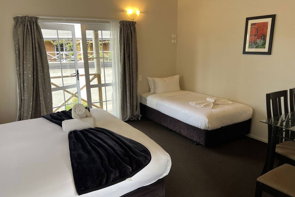 A hotel room with a large bed, a smaller bed, a chair, and a window with curtains.