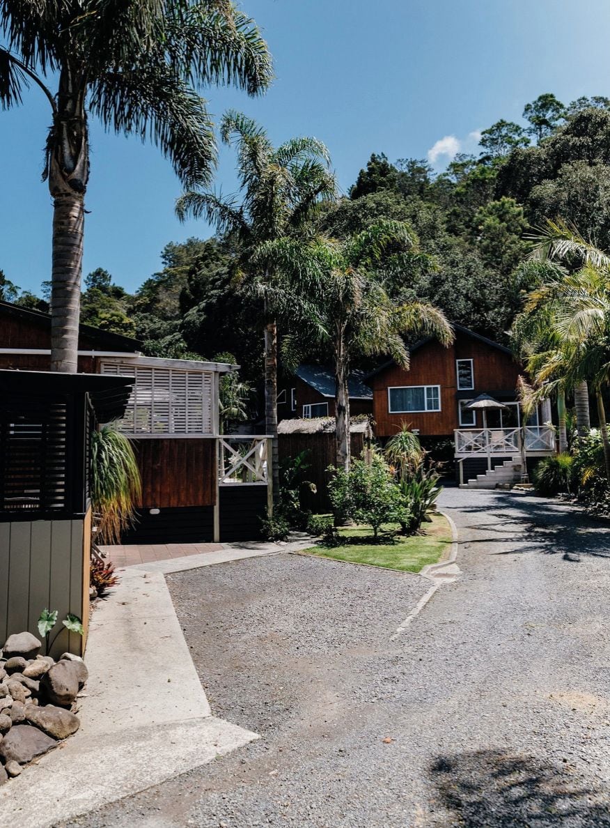 A residential area with a gravel driveway leading to a wooden house with a balcony.