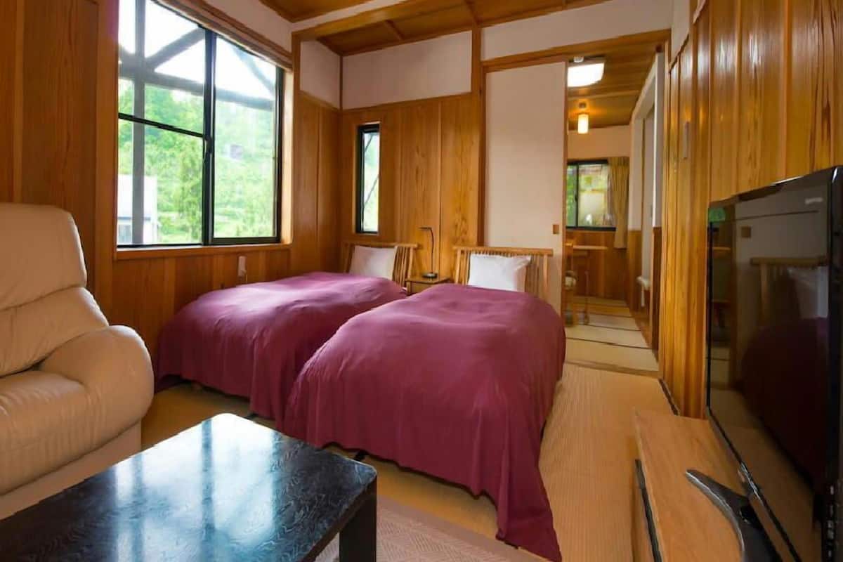 A cabin with a wooden interior, two beds with purple bedding, a TV, and a dining area.
