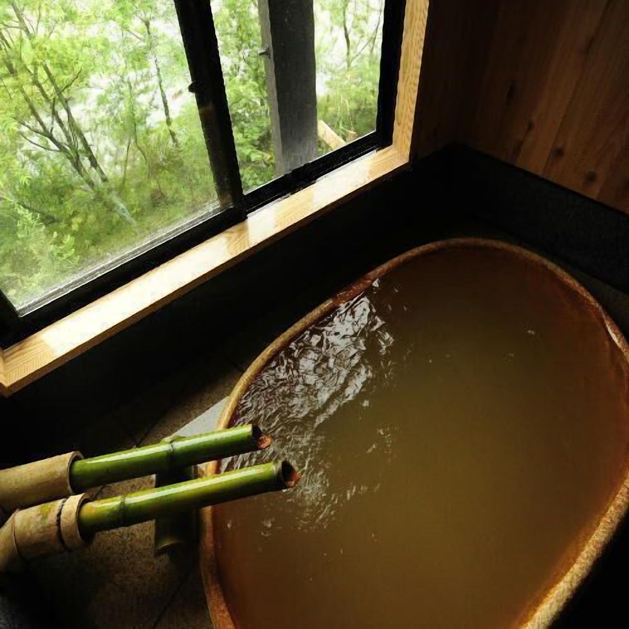 A wooden bathtub with a window view of a forest.