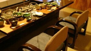 A dining table with various dishes and bowls, wooden chairs, and a window in the background. - Motokawarayu (Okura)