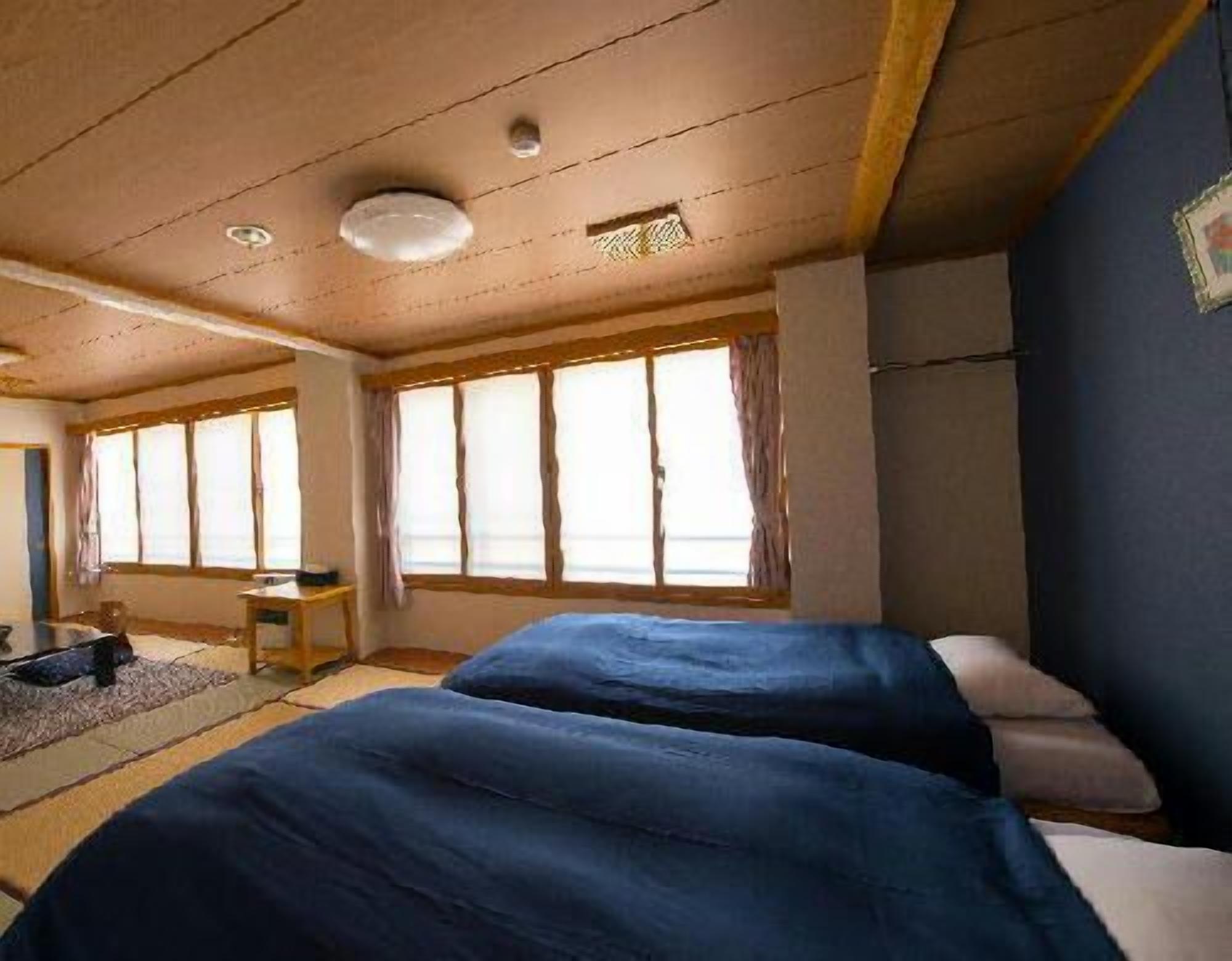 A room with two beds, a desk, and large windows.