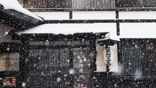 A traditional Japanese building with a snow-covered roof and a sign with Japanese characters. - Motokawarayu (Okura)