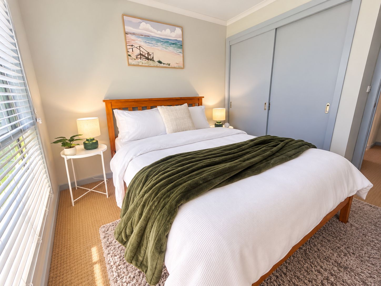 A bedroom with a bed, bedside tables, a nightstand, a painting, and a door.