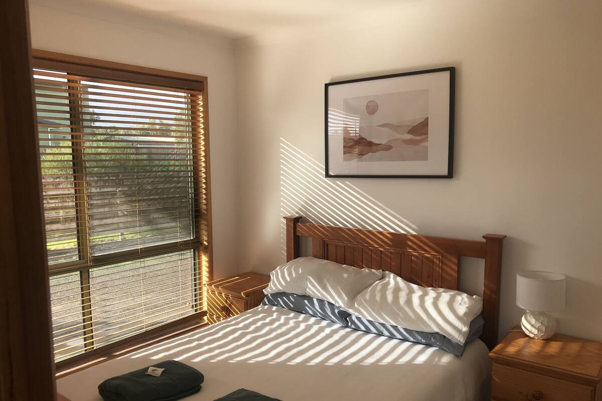 A neatly made bed with striped bedding, a wooden headboard, and two towels on the bedside table.
