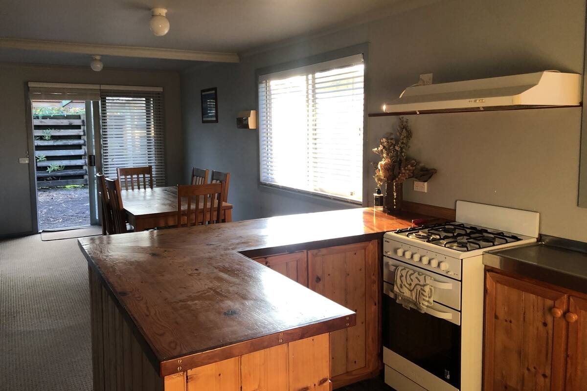 A kitchen with a wooden countertop, a stove, and a dining area with chairs and a table.