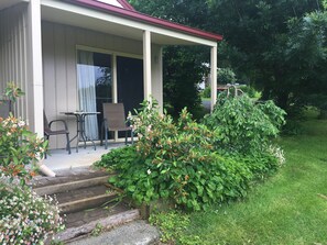 A covered porch with a table and chairs, surrounded by greenery and a small garden. - Neerim Country Cottages (Neerim South)