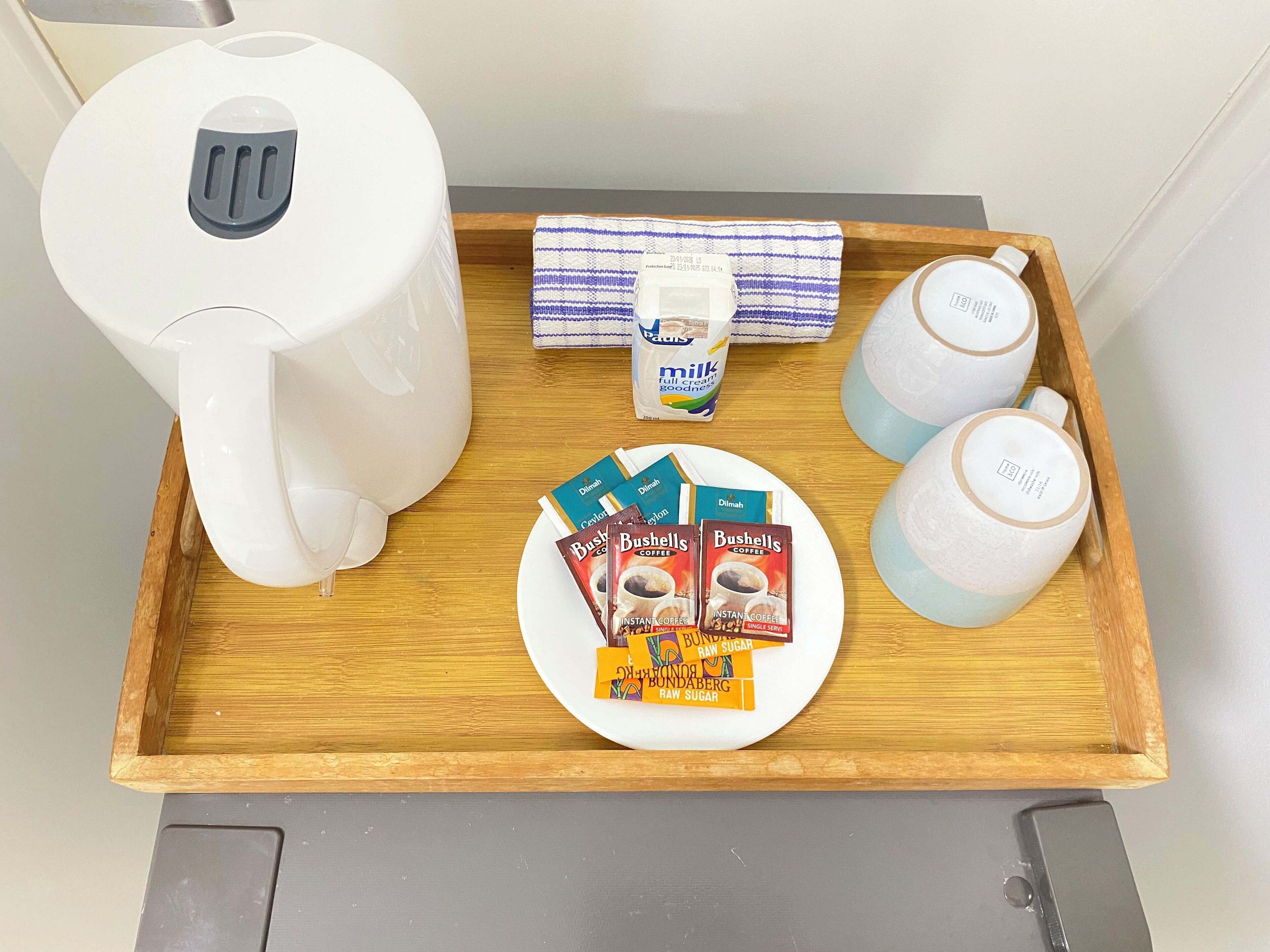 Un plateau contenant une machine à café, un carton de lait, des sachets de café et deux tasses.