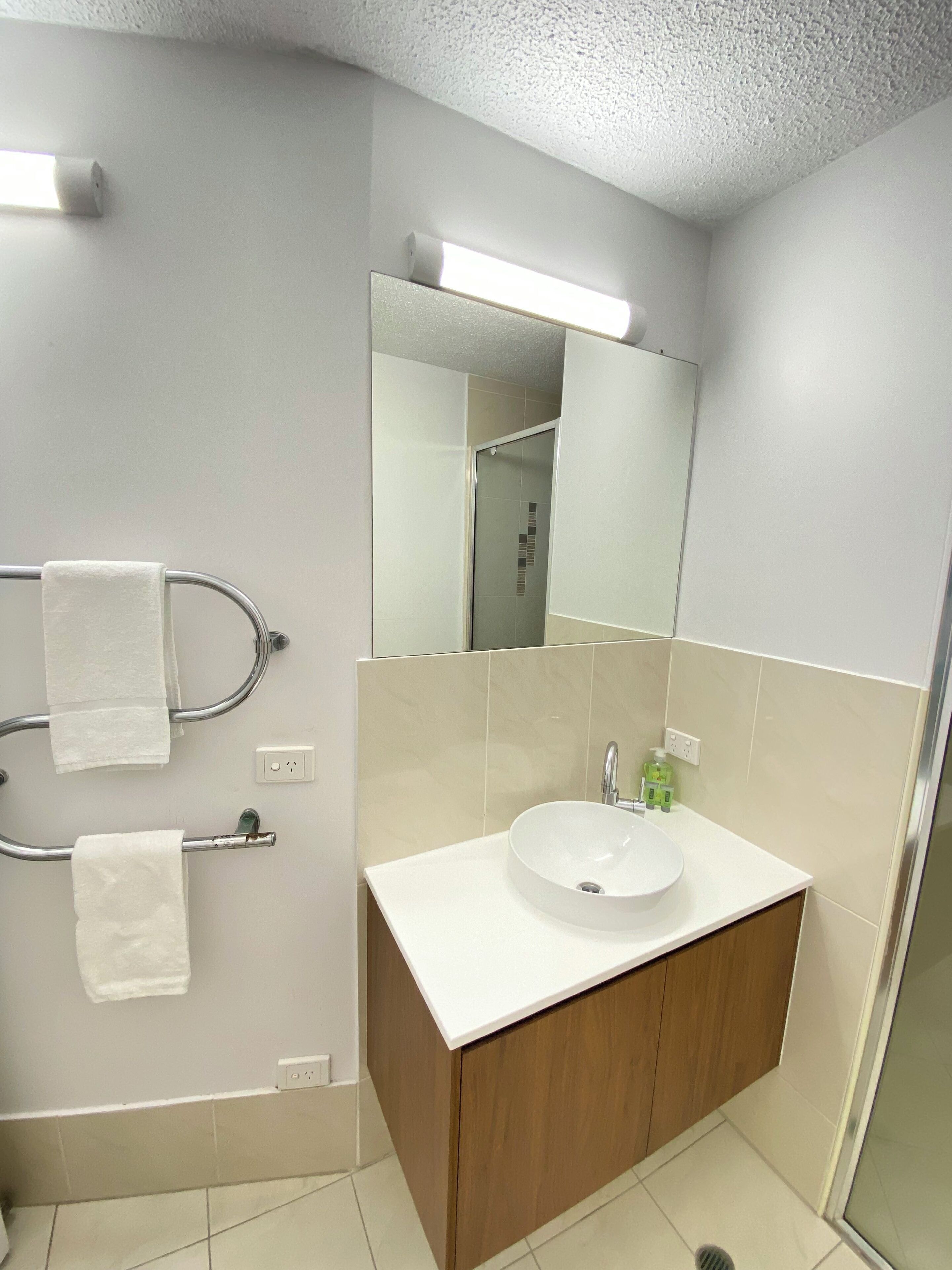 A modern bathroom with a white sink, wooden cabinets, and a large mirror.