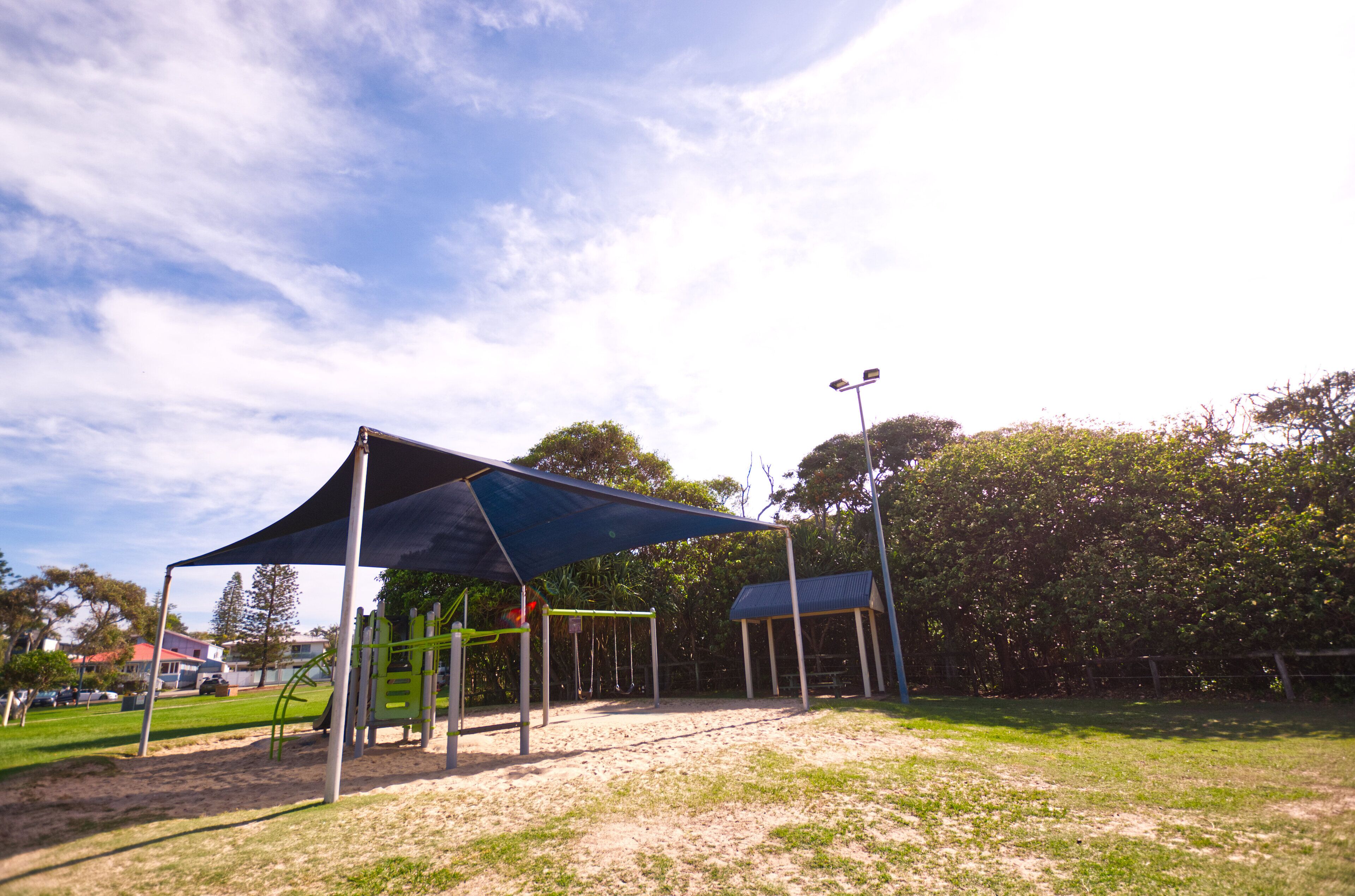 A playground with a shaded area, swings, and a fenced enclosure.