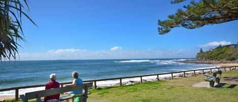 A bench overlooking a beach with ocean views, a grassy area, and a wooden railing.