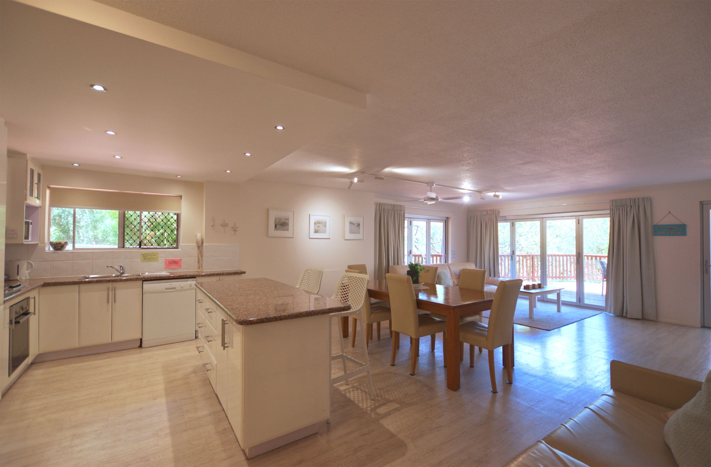 A modern kitchen with a dining area, large windows, and a ceiling fan.