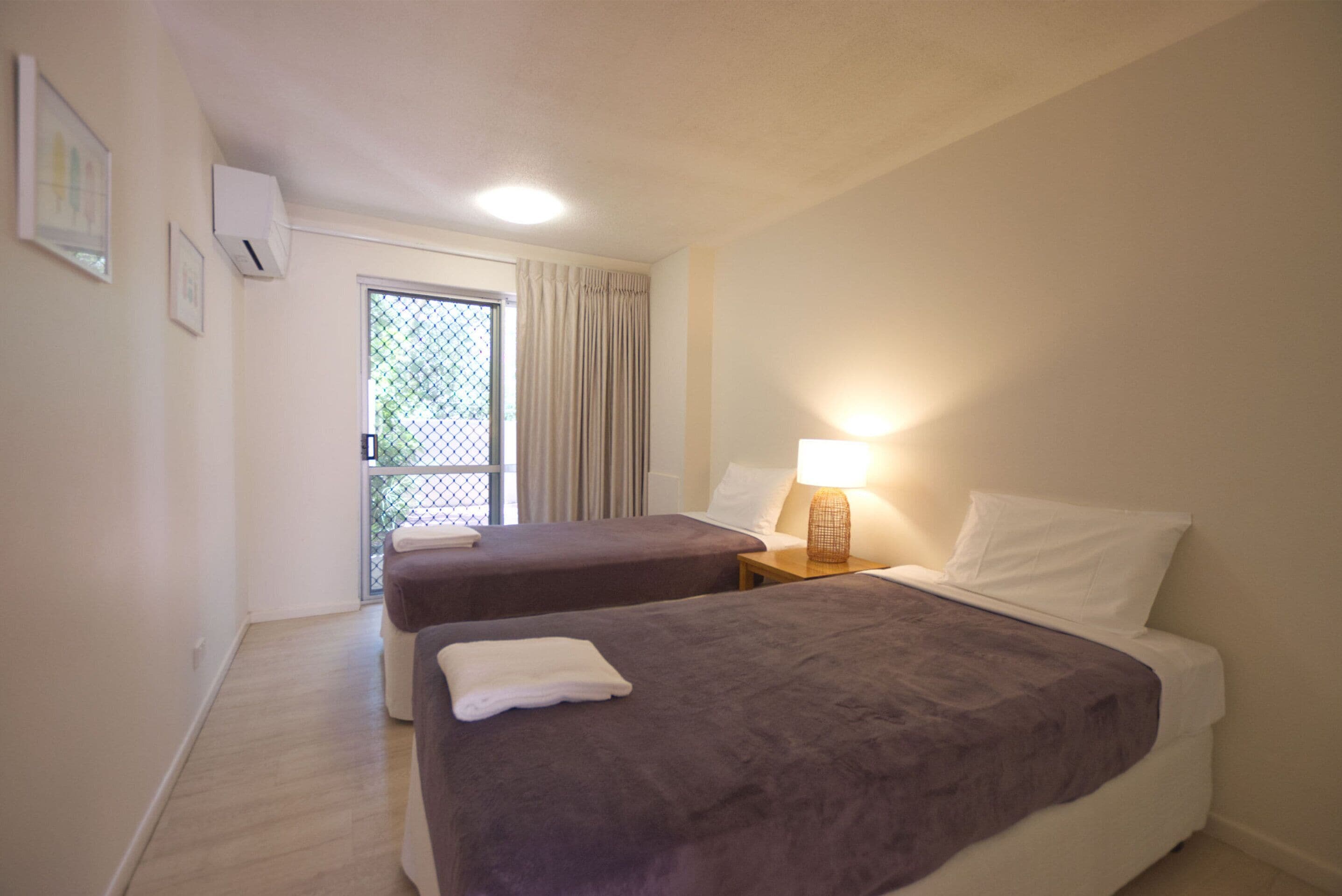 Habitación de hotel con dos camas, una ventana con cortinas, una lámpara de noche y aire acondicionado instalado en la pared.
