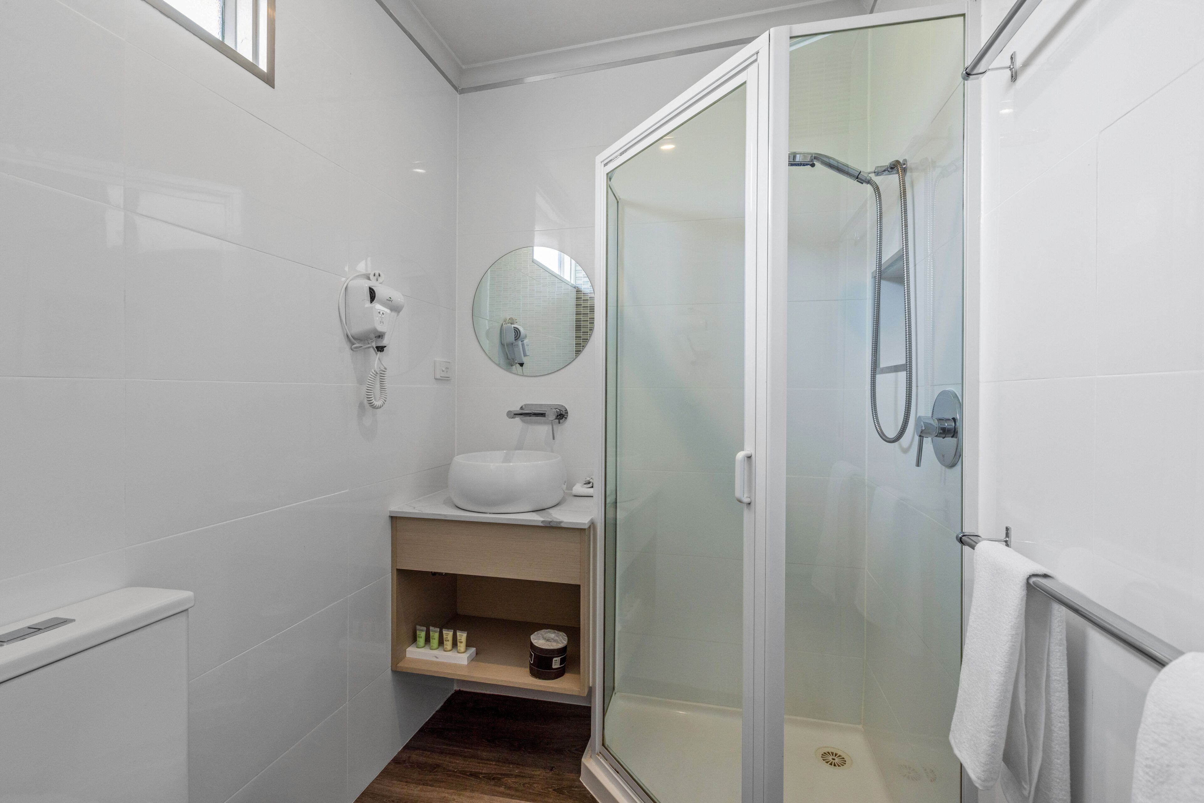 Een moderne badkamer met een douchecabine van glas, een witte wastafel, een spiegel en een aan de muur bevestigde haardroger.