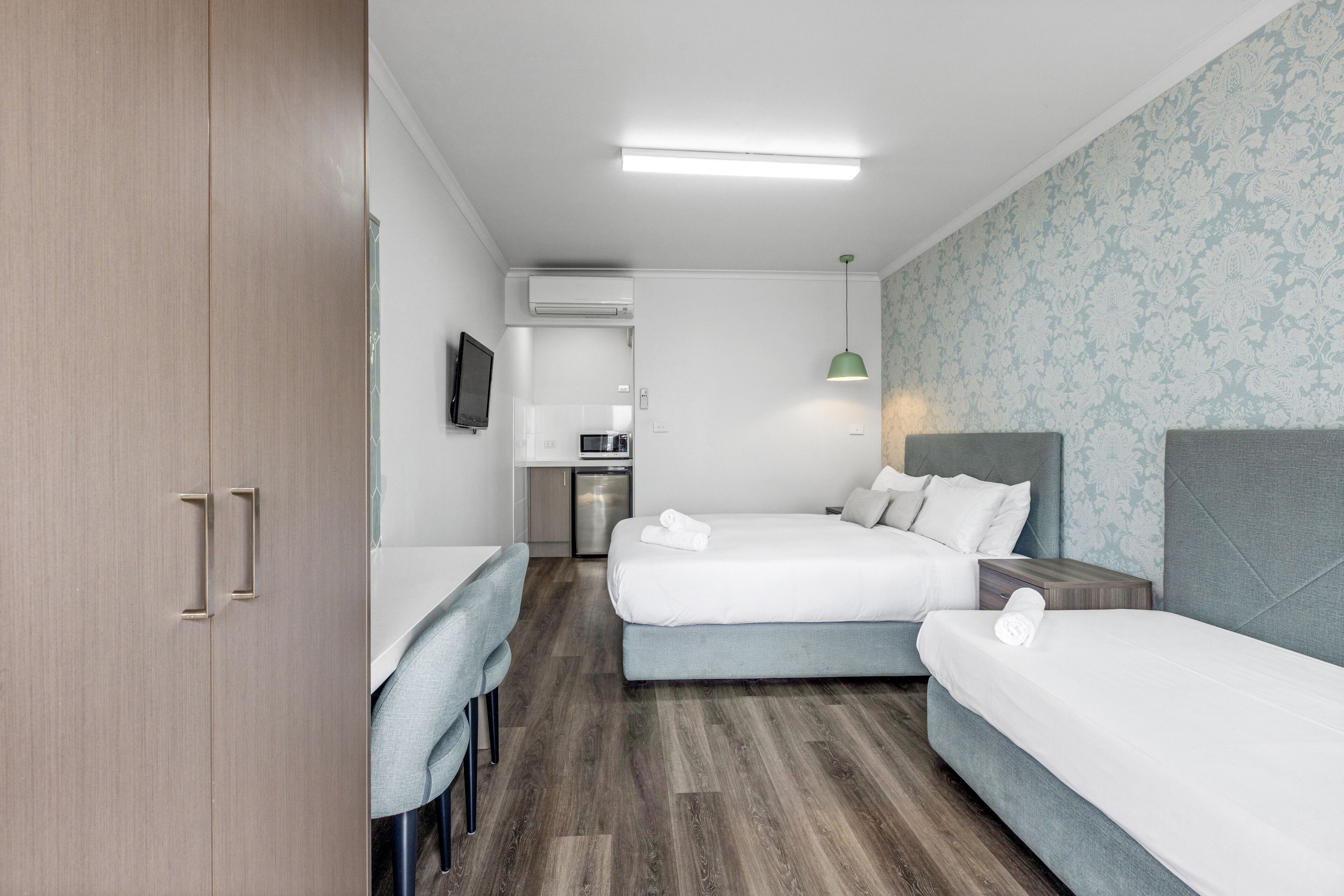 Una habitación de hotel moderna con dos camas, un escritorio y una kitchenette.