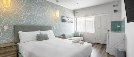 Un dormitorio moderno con una cama grande, una mesita de noche, un televisor montado en la pared y un ventanal con cortinas.
