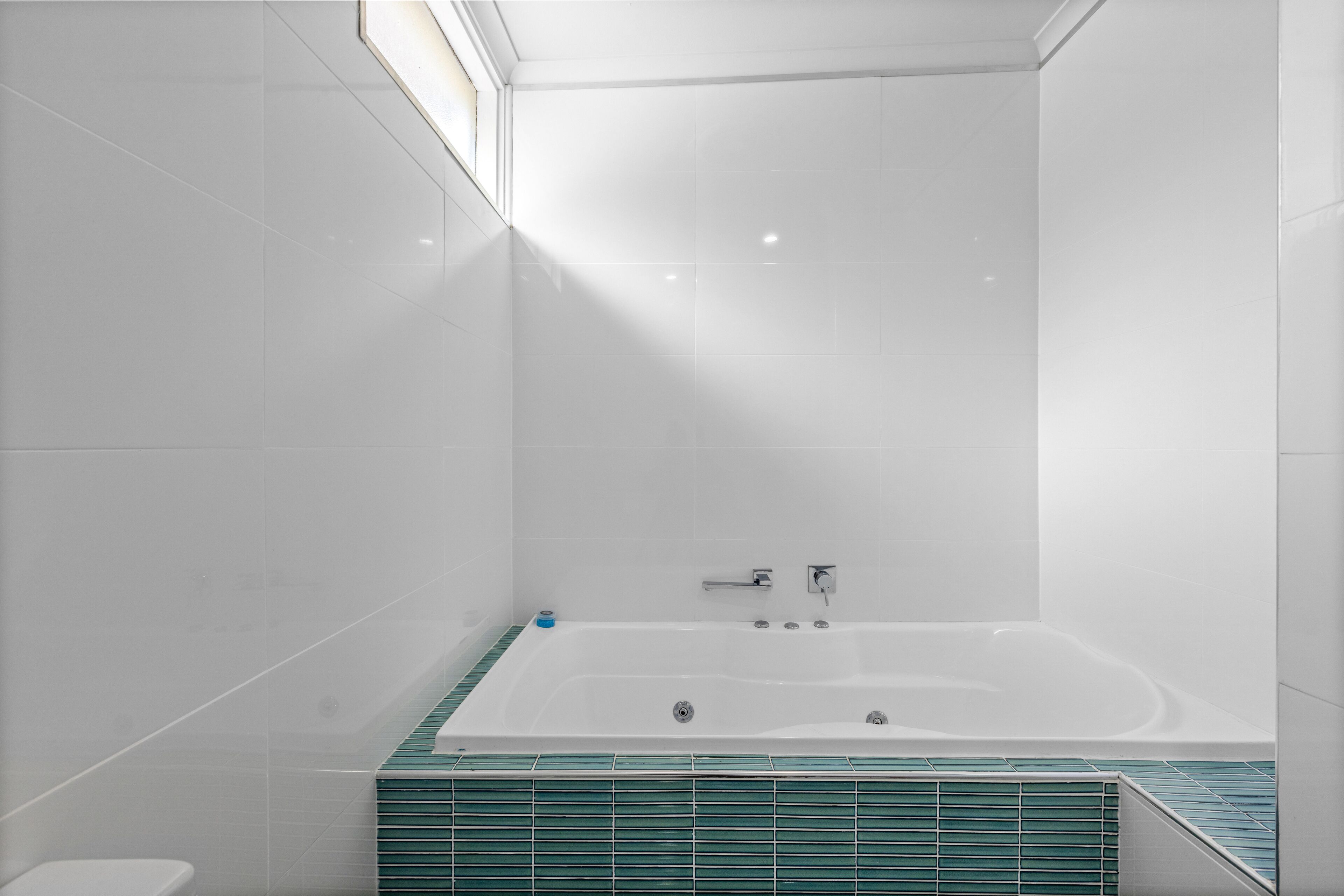 A modern bathroom with a large bathtub, white tiles, and a green-tiled shower area.