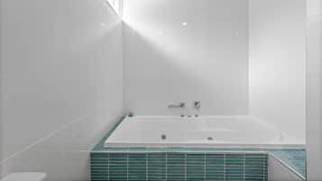 A modern bathroom with a large bathtub, white tiles, and a green-tiled shower area.