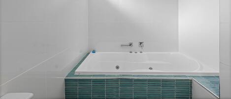 A modern bathroom with a large bathtub, white tiles, and a green-tiled shower area.