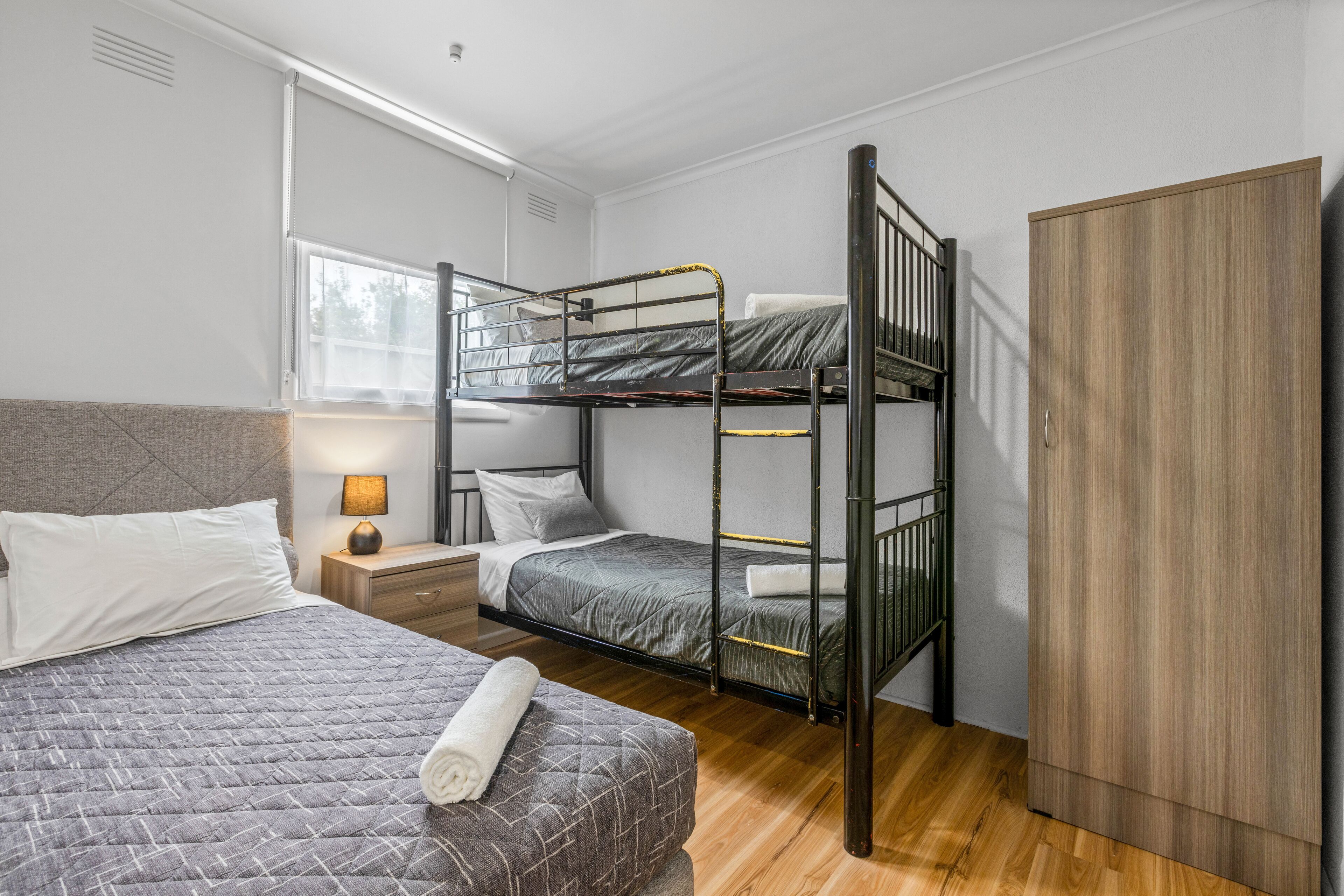 Een kamer met stapelbedden, een houten garderobe, een nachtkastje met een lamp en een gewatteerde sprei.