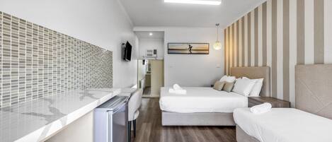 A hotel room with a kitchenette, two beds, a TV, and a painting on the wall.