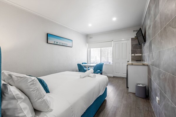 Habitación de hotel con cama, escritorio, silla, kitchenette y ventana.
