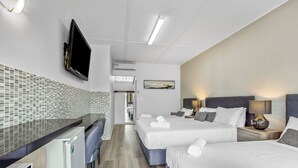 Habitación de hotel con dos camas, un escritorio, un televisor y un baño a la vista a través de una puerta abierta.