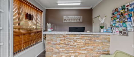 A reception area with a sign for Rosebud Motel, a counter with a stone mosaic, a reception desk, and a wall with various brochures.