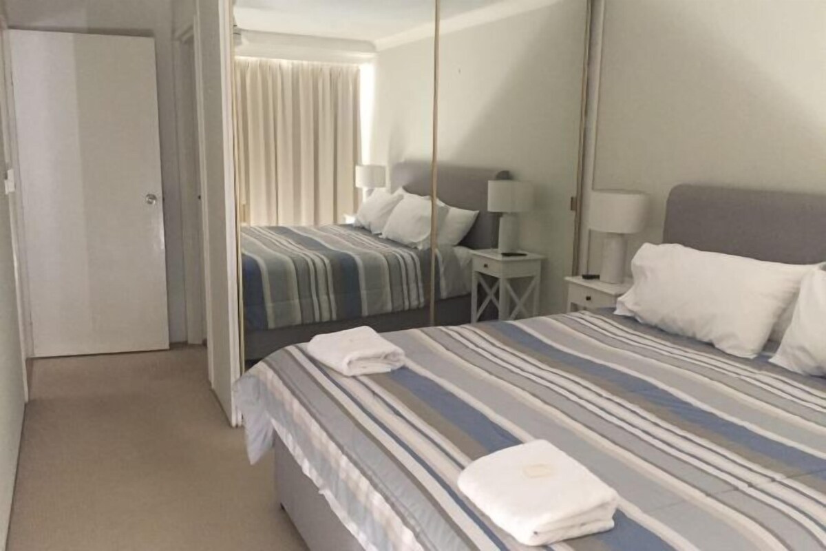 Una habitación de hotel con una cama, una mesita de noche, una lámpara y un espejo.