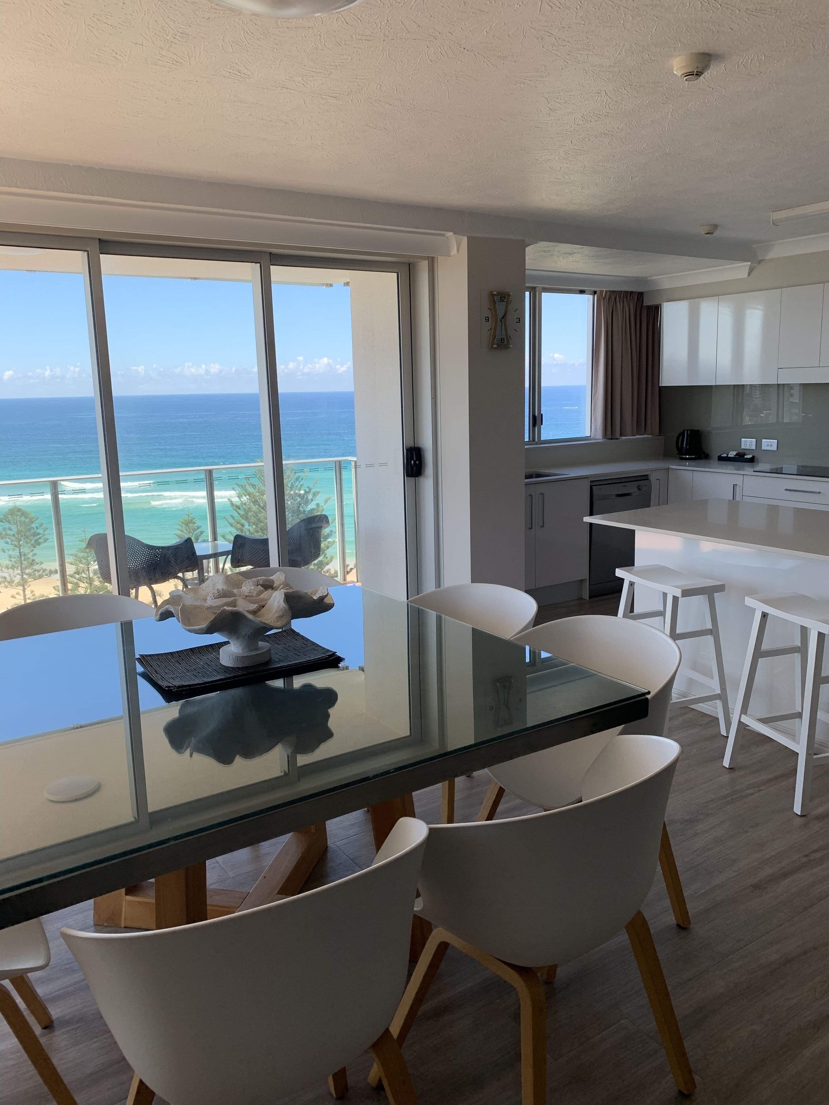 Een moderne keuken met witte kasten, een eetgedeelte met een glazen tafel en uitzicht op de oceaan.