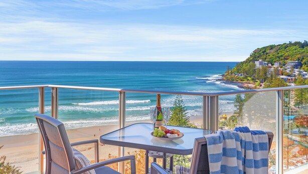 A balcony with a table, chairs, and a view of the ocean and beach. - Pacific Regis Apartments (Burleigh Heads)