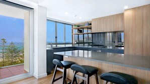 A modern kitchen with a large island, bar stools, and a view of the city. - Pacific Regis Apartments (Burleigh Heads)
